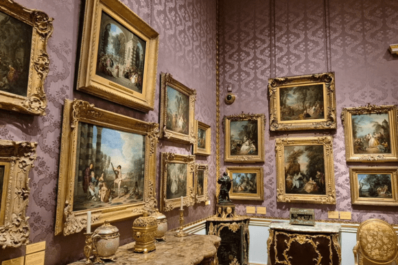 Gallery wall at The Wallace Collection in London displaying an extensive collection of framed Rococo and Old Master paintings in ornate gold frames above antique furniture and decorative art pieces.