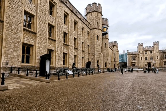 Historic courtyard inside the Tower of London featuring medieval stone buildings, fortified towers, cannons, and visitors exploring the royal fortress.