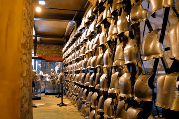 Historic suits of medieval armour displayed inside the Tower of London museum, featuring rows of steel breastplates and helmets in a stone-walled gallery.