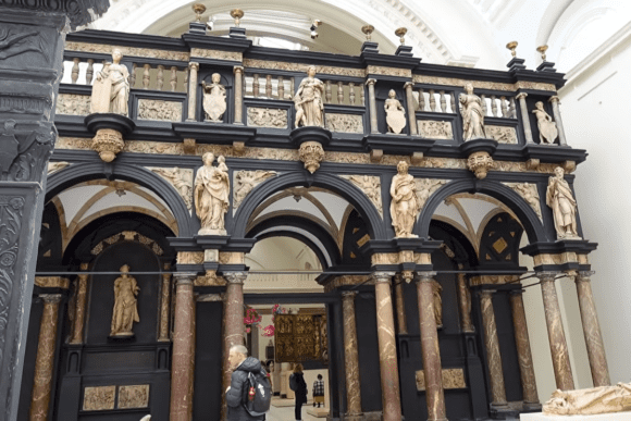 Ornate Renaissance-style gallery inside the Victoria and Albert Museum in London, featuring marble columns, classical statues, decorative arches, and historic architectural details.