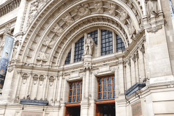 Grand entrance facade of the Victoria and Albert Museum in London, featuring ornate Victorian architecture, carved stone arches, statues, and historic museum doors.
