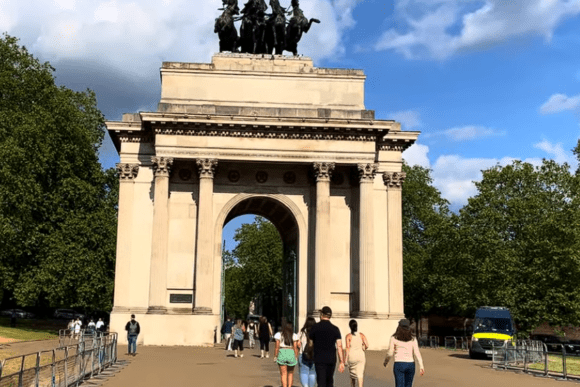 Wellington Arch in London with visitors walking beneath the grand stone archway, topped by the famous bronze quadriga sculpture against a bright blue sky.