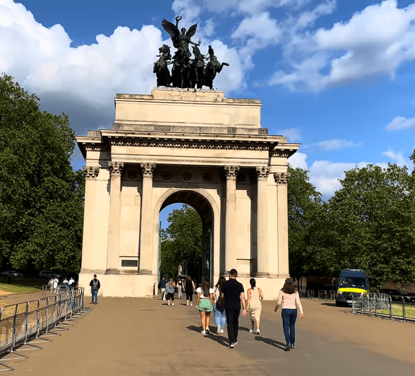 Wellington Arch in London with visitors walking beneath the grand stone archway, topped by the famous bronze quadriga sculpture against a bright blue sky.