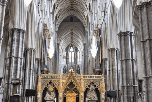 Interior view of Westminster Abbey in London featuring soaring Gothic arches, towering stone columns, ornate chandeliers, and the grand high altar beneath vaulted ceilings.