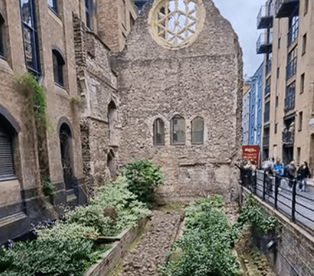Ruins of Winchester Palace in Southwark, London, featuring medieval stone walls, Gothic windows, and the famous rose window above a historic garden courtyard.