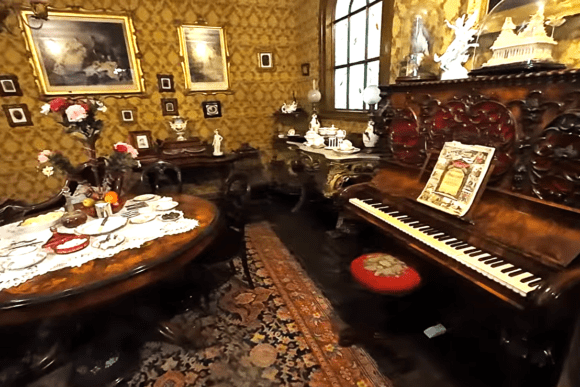 Victorian parlour recreation inside York Castle Museum featuring an ornate upright piano, antique dining furniture, decorative wallpaper, framed artwork, and authentic 19th-century home furnishings.
