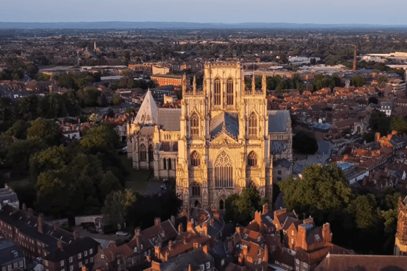 Aerial view of York Minster cathedral rising above the historic city of York, featuring Gothic towers, medieval architecture, and surrounding rooftops at sunset.