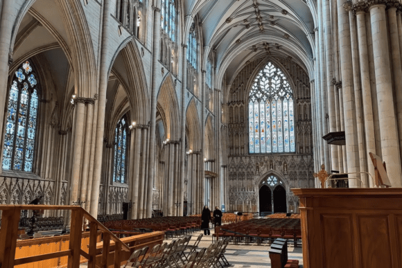 Interior of York Minster featuring soaring Gothic arches, stained glass windows, stone columns, and the grand nave of the historic cathedral in York, England.
