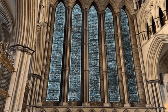 Tall stained glass windows inside York Minster framed by soaring Gothic arches and intricate medieval stone architecture in York, England.