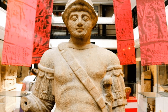 Ancient Roman stone statue displayed inside Yorkshire Museum, surrounded by archaeological exhibits and striking red banners highlighting York’s Roman heritage and historical collections.