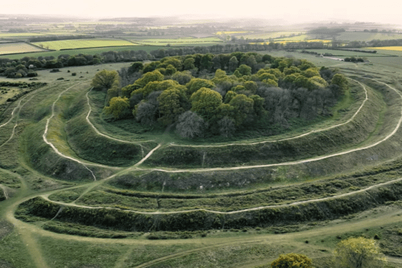 Aerial view of Badbury Rings Iron Age hill fort with concentric earthworks and woodland in Dorset