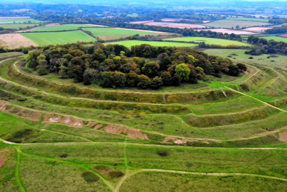 Wide aerial view of Badbury Rings Iron Age hill fort with triple earthwork ramparts and surrounding farmland in Dorset