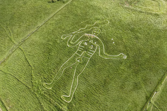 Aerial view of the Cerne Abbas Giant chalk hill figure on a green hillside, showing the full outline of the naked figure holding a raised club.