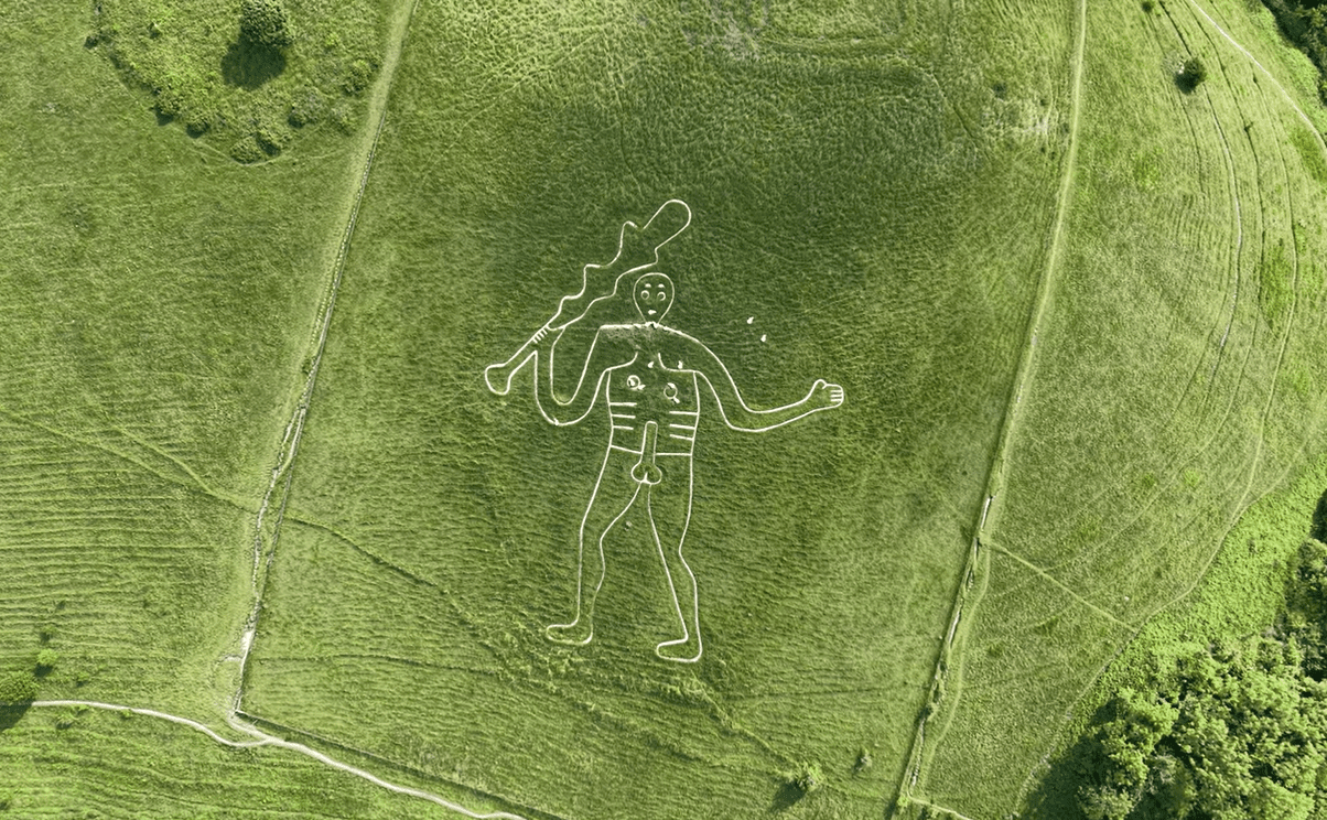 Aerial view of the Cerne Abbas Giant chalk hill figure carved into a green hillside, depicting a large naked man holding a club.