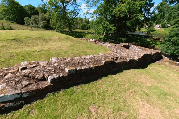 Stone remains of Chesters Bridge Abutment on Hadrian’s Wall set in grassy landscape beside the River North Tyne.