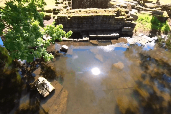Chesters Bridge Abutment on Hadrian’s Wall beside the River North Tyne, showing Roman stone ruins reflected in shallow water.