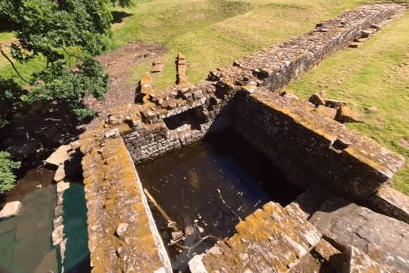 Aerial view of Chesters Bridge Abutment on Hadrian’s Wall showing Roman stone foundations and water-filled structure.