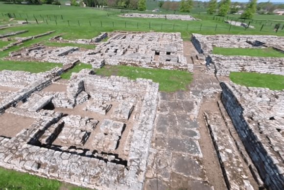 Stone ruins of Chesters Roman Fort on Hadrian’s Wall, showing excavated foundations and pathways in open countryside.