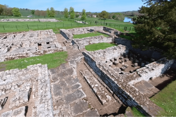 Aerial view of Chesters Roman Fort ruins on Hadrian’s Wall, showing stone foundations, streets, and surrounding countryside.