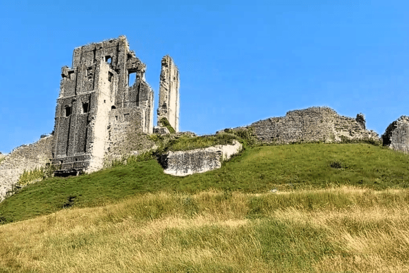 The ruined towers of Corfe Castle on a grassy hill under a clear blue sky in Dorset.