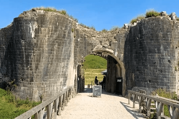 The stone gatehouse entrance to Corfe Castle with twin round towers and a wooden footbridge under a blue sky.