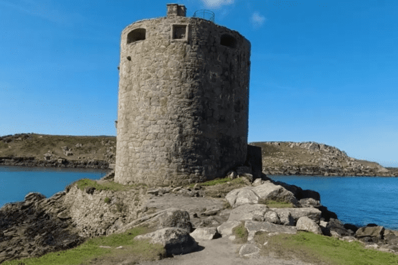 Cylindrical stone tower of Cromwell’s Castle standing on a rocky headland beside the sea.
