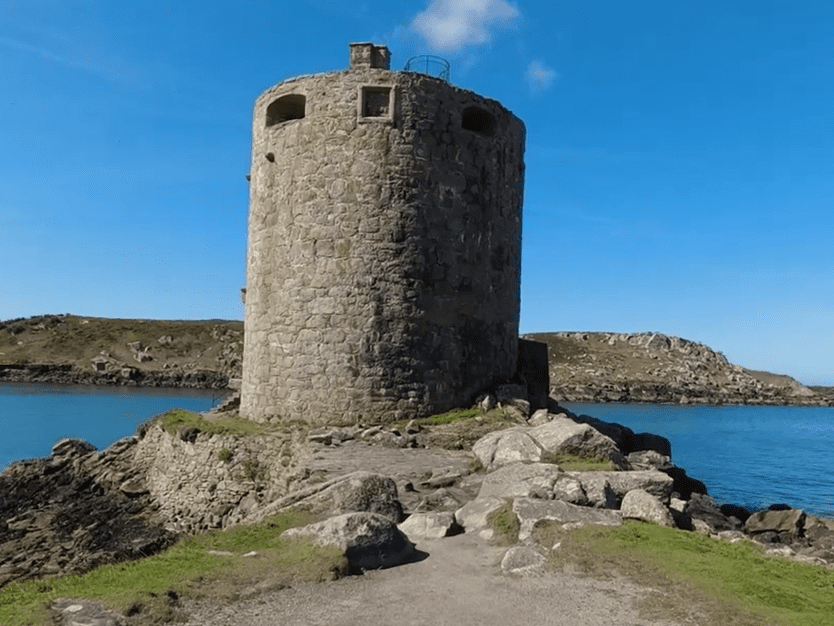 Cylindrical stone tower of Cromwell’s Castle standing on a rocky headland beside the sea.