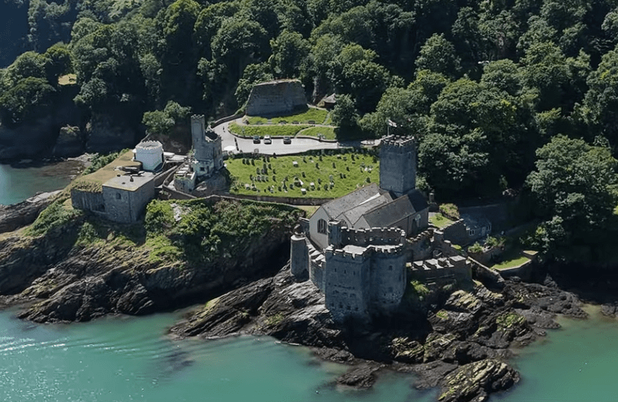 Aerial view of Dartmouth Castle on a rocky headland surrounded by woodland and turquoise waters of the River Dart.