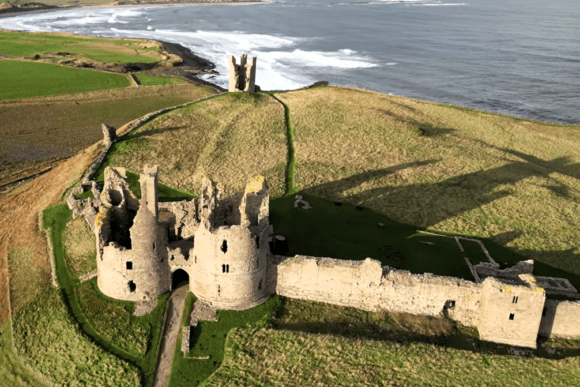 Aerial view of Dunstanburgh Castle ruins on a grassy headland overlooking the North Sea.