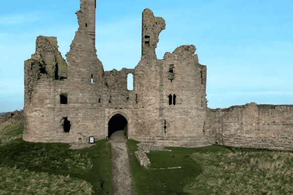 Front view of the ruined gatehouse at Dunstanburgh Castle with broken towers and arched entrance.