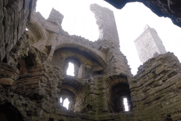 Interior view of Dunstanburgh Castle showing arched stone walls and towering ruined structures above.