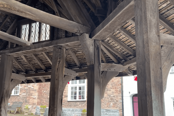 Interior view of Dunster Yarn Market showing heavy timber posts, beams, and the underside of the shingled roof.