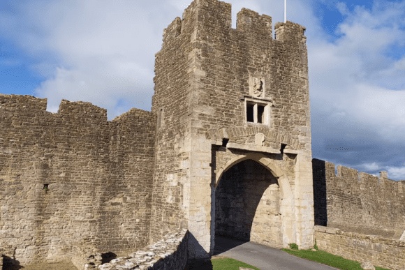 Stone gatehouse and arched entrance at Farleigh Hungerford Castle, with crenellated walls under a partly cloudy sky.