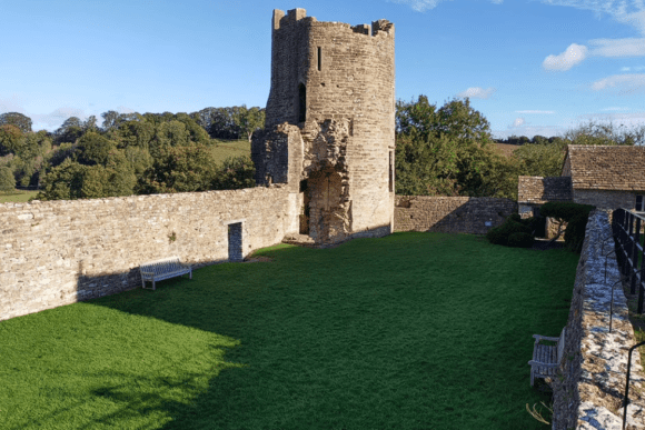 Round stone tower and inner courtyard at Farleigh Hungerford Castle, with grassy lawn enclosed by medieval walls.