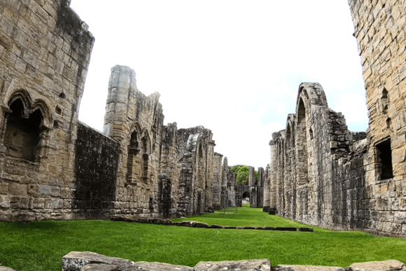 Long stone walls and arches of Finchale Priory forming a grassy central nave under an open sky.