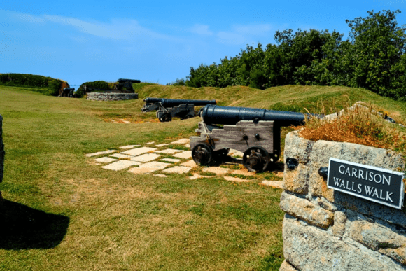 Historic cannons positioned along grassy garrison walls with a stone sign reading “Garrison Walls Walk.”