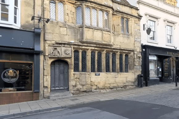 Historic stone façade of the Glastonbury Tribunal building with leaded windows and an arched doorway along a town street.