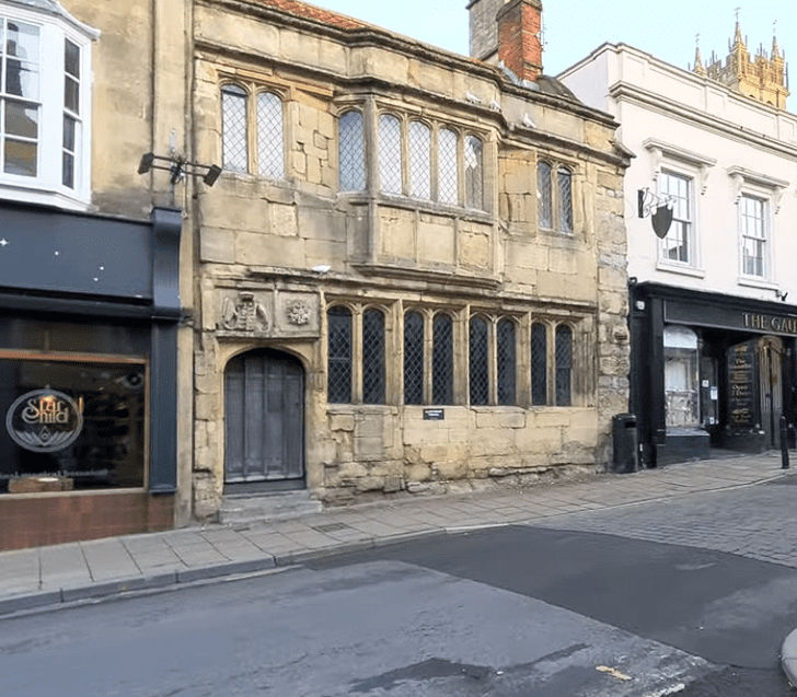 Historic stone façade of the Glastonbury Tribunal building with leaded windows and an arched doorway along a town street.