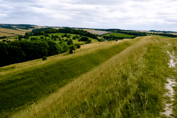 Grassy ramparts and walking path along the earthworks of Hod Hill hillfort in Dorset.