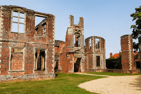 Ruins of Houghton House with red brick walls, tall chimneys, and open window frames in Bedfordshire.