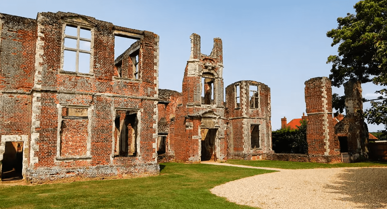Ruins of Houghton House with red brick walls, tall chimneys, and open window frames in Bedfordshire.