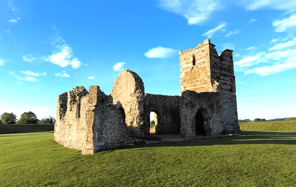 Ruins of Knowlton Church standing in an open grassy field under a blue sky.