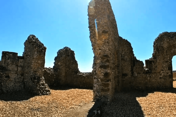 Interior ruins of Knowlton Church with stone walls and arches under a bright sky.