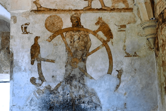 Medieval wall painting inside Longthorpe Tower showing a crowned figure within a wheel surrounded by animals.
