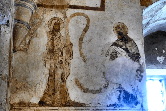 Faded medieval wall paintings in Longthorpe Tower showing two haloed figures on a plaster wall.