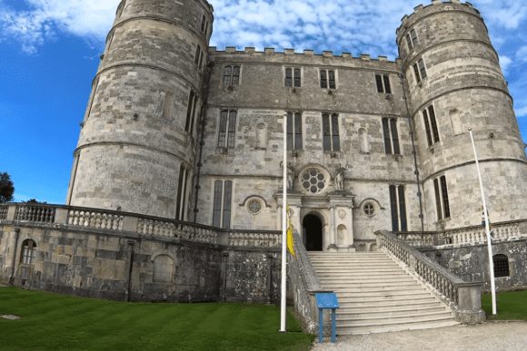 Front view of Lulworth Castle with twin round towers, stone steps, and entrance under a blue sky.