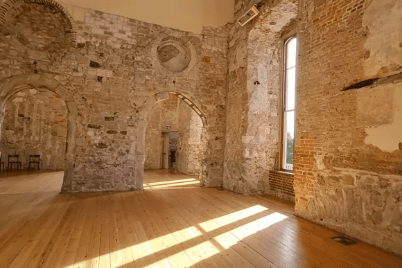 Interior hall of Lulworth Castle with exposed stone walls, arched doorways, and sunlight on wooden floor.