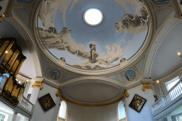 Painted dome ceiling inside Lulworth Castle with a central skylight and decorative figures among clouds.