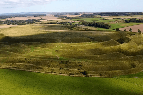 Aerial view of Maiden Castle showing large earthwork ramparts and surrounding countryside.
