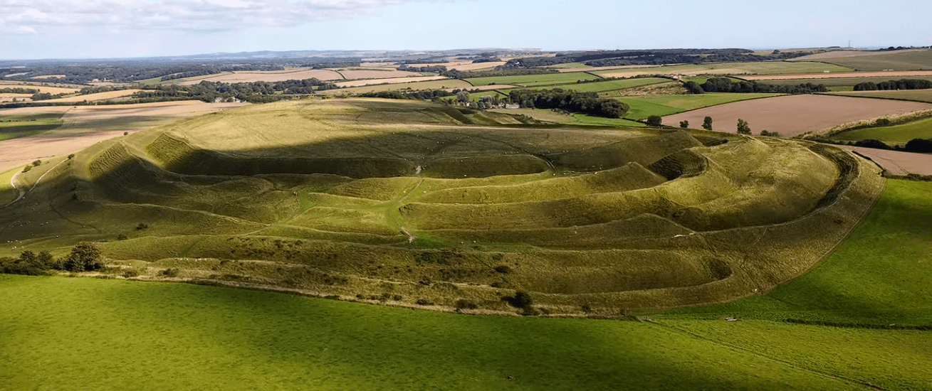 Aerial view of Maiden Castle showing large earthwork ramparts and surrounding countryside.